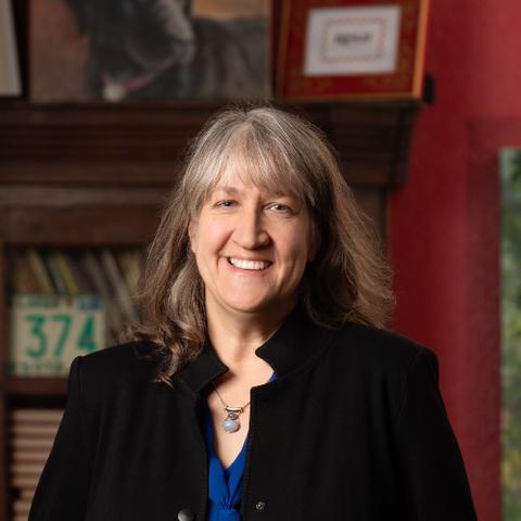A woman with shoulder-length gray hair, wearing a black blazer and blue blouse 