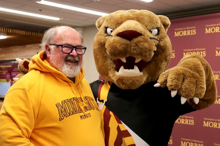 Alum posing and smiling with Pounce, the cougar mascot